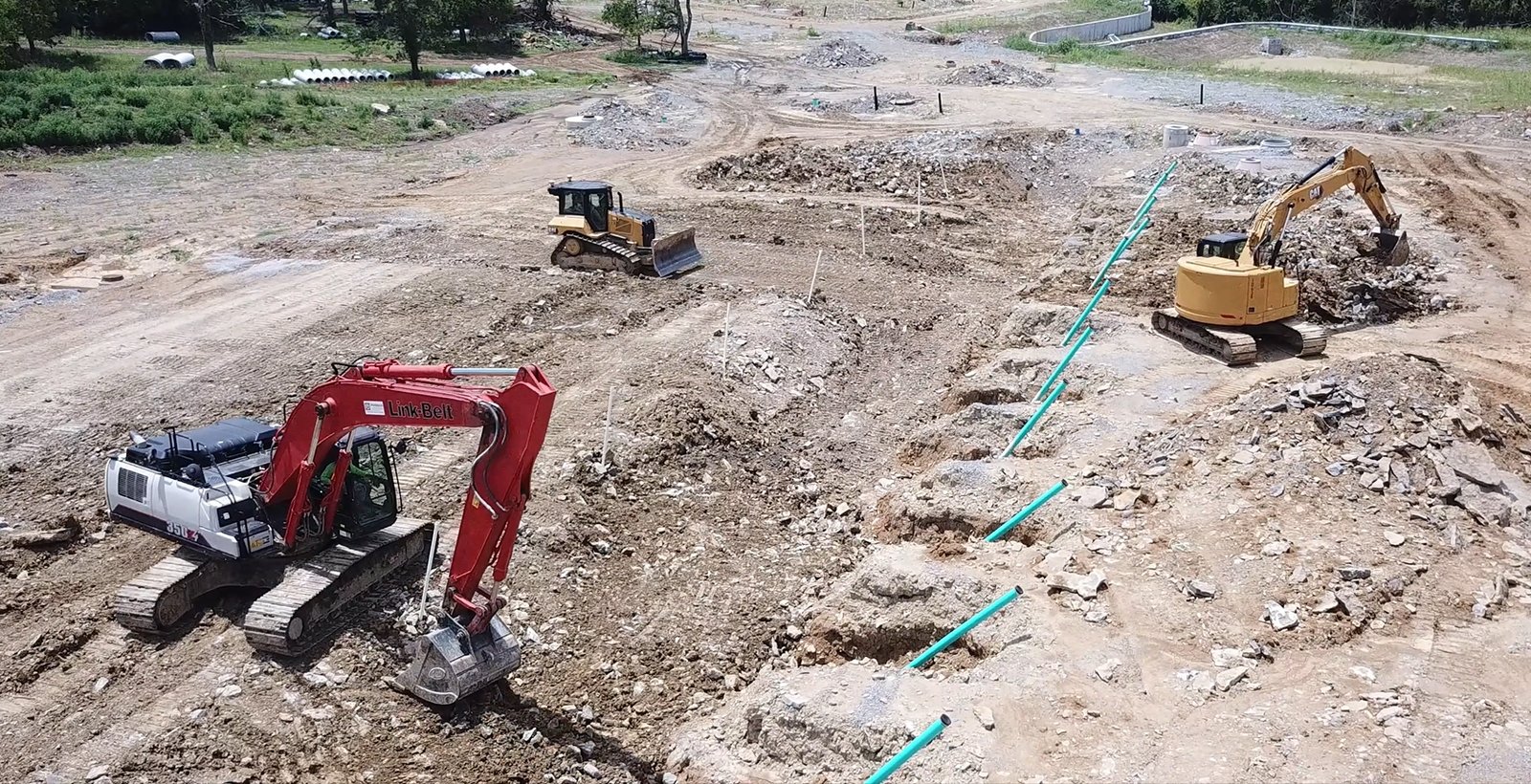 Aerial view of an active PMT Site civil project with multiple excavators, a dozer, and underground utility trenches